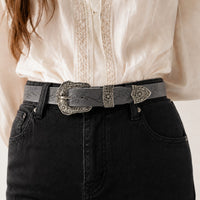 Ceinture large western La Ceinture Pour Femme en cuir gris avec boucle ciselée argentée portée sur un jean noir
